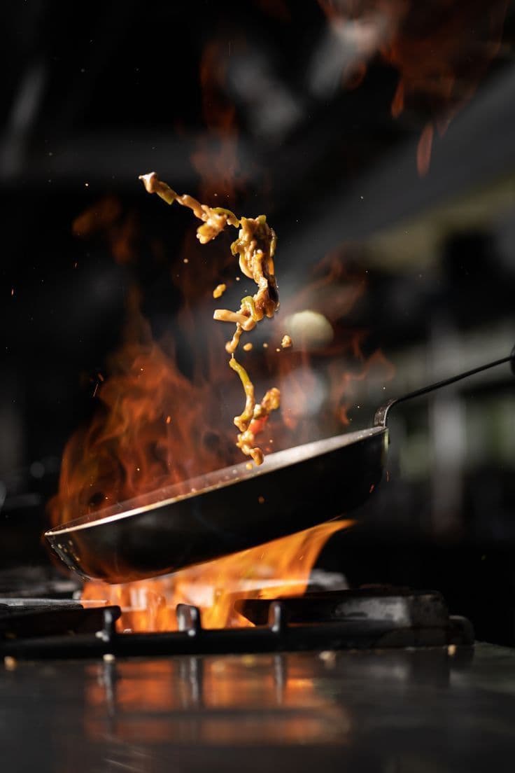 Flames rising from a pan as a stir-fry is tossed over an open flame